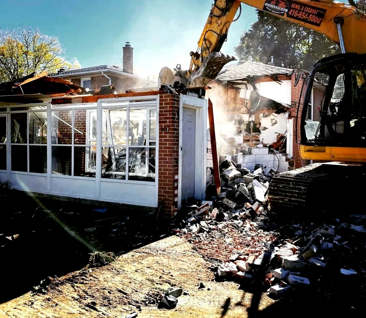 Excavator pulling down a brick bungalow with a glazed sunroom