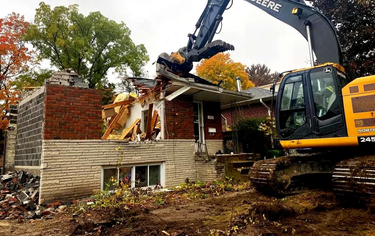 Yellow excavator at work on a brick house in autumn