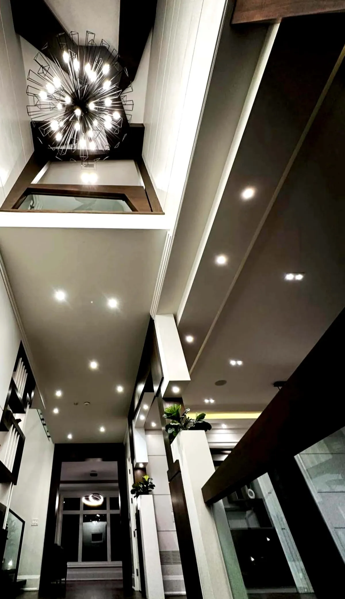 Long entrance hall seen from above with a burst chandelier and layered ceiling