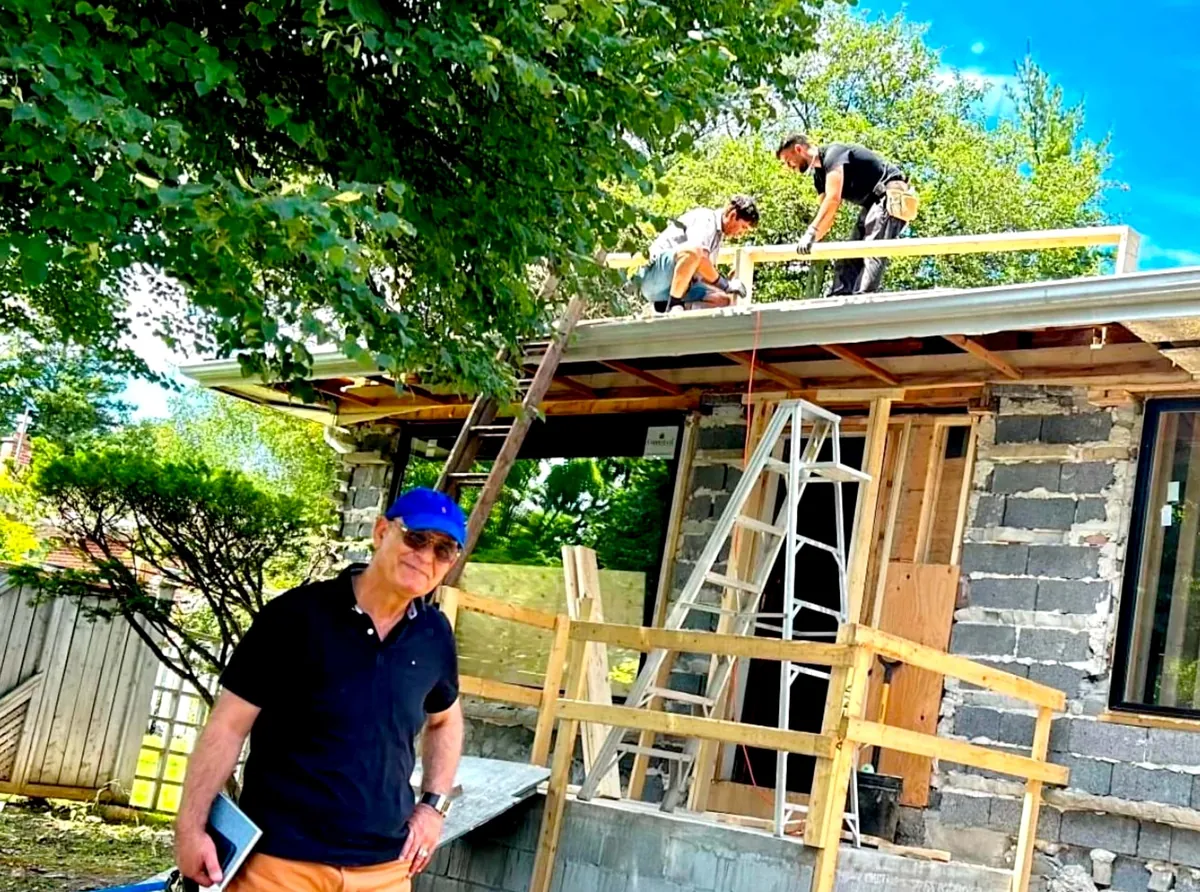 Kambiz Divanbeigi on site in a blue cap in front of a block-and-timber facade being rebuilt