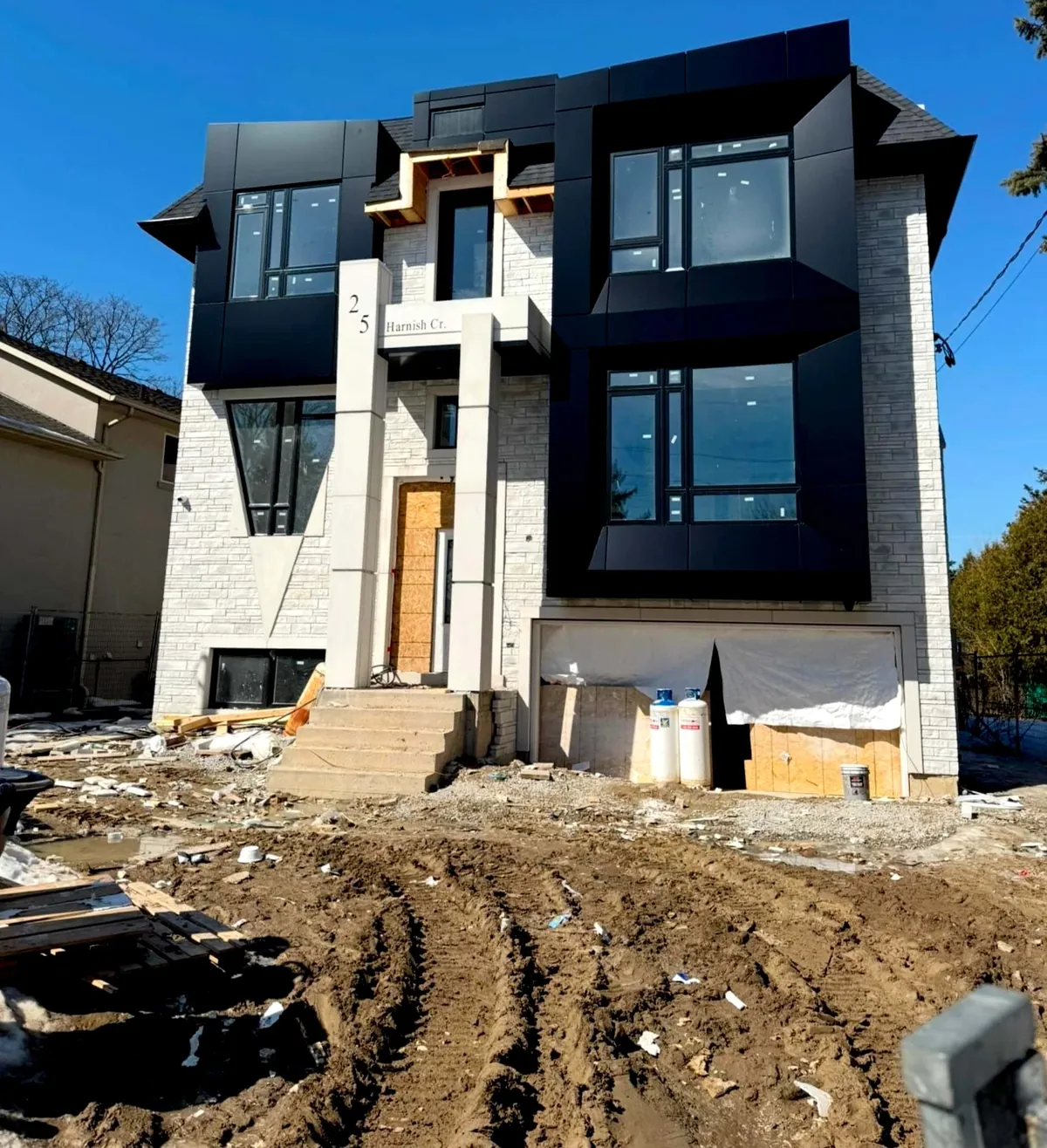 Black metal-clad and pale stone front elevation of a new house under a deep blue sky