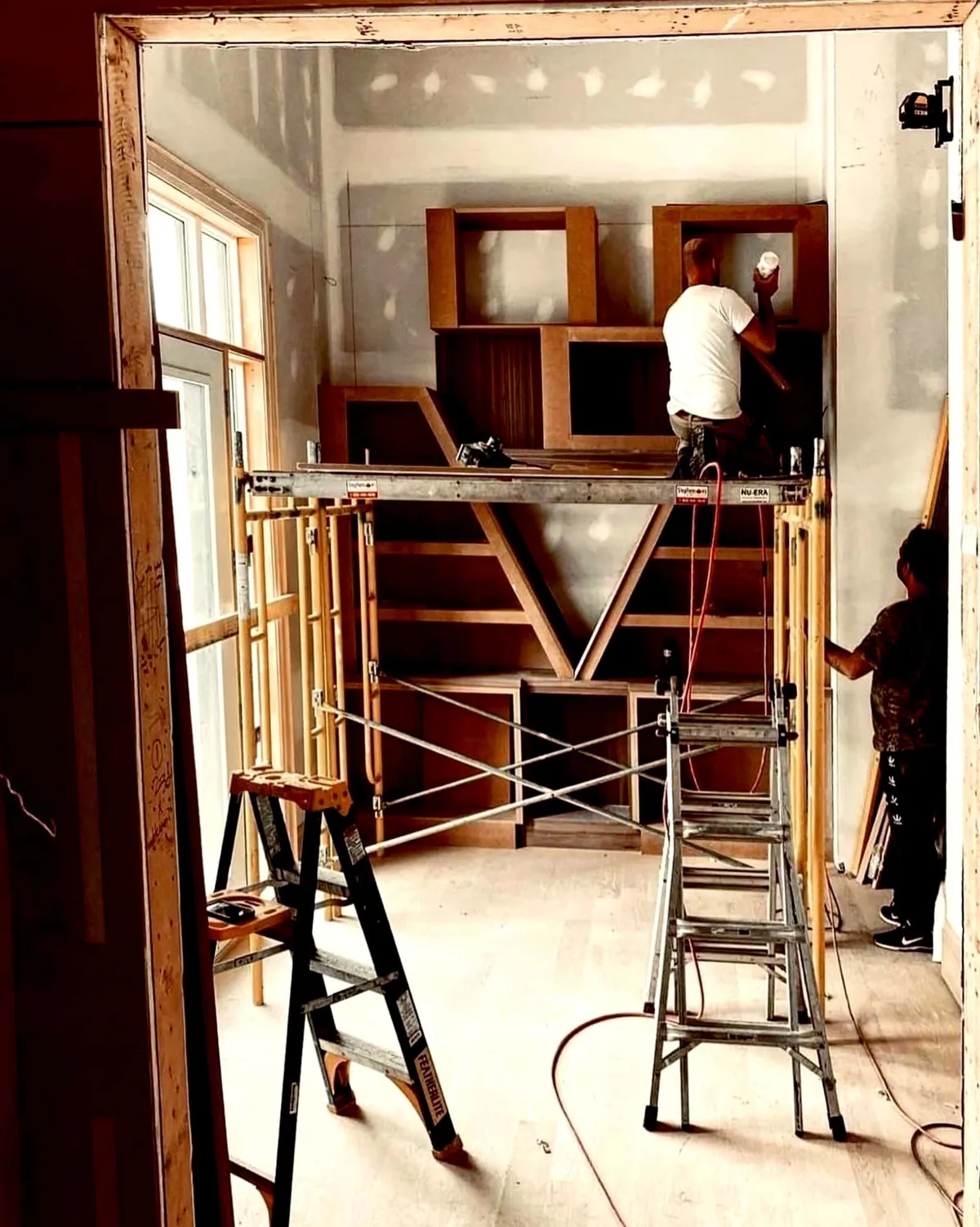 Crew on scaffolding fitting built-in library shelving in an unfinished room