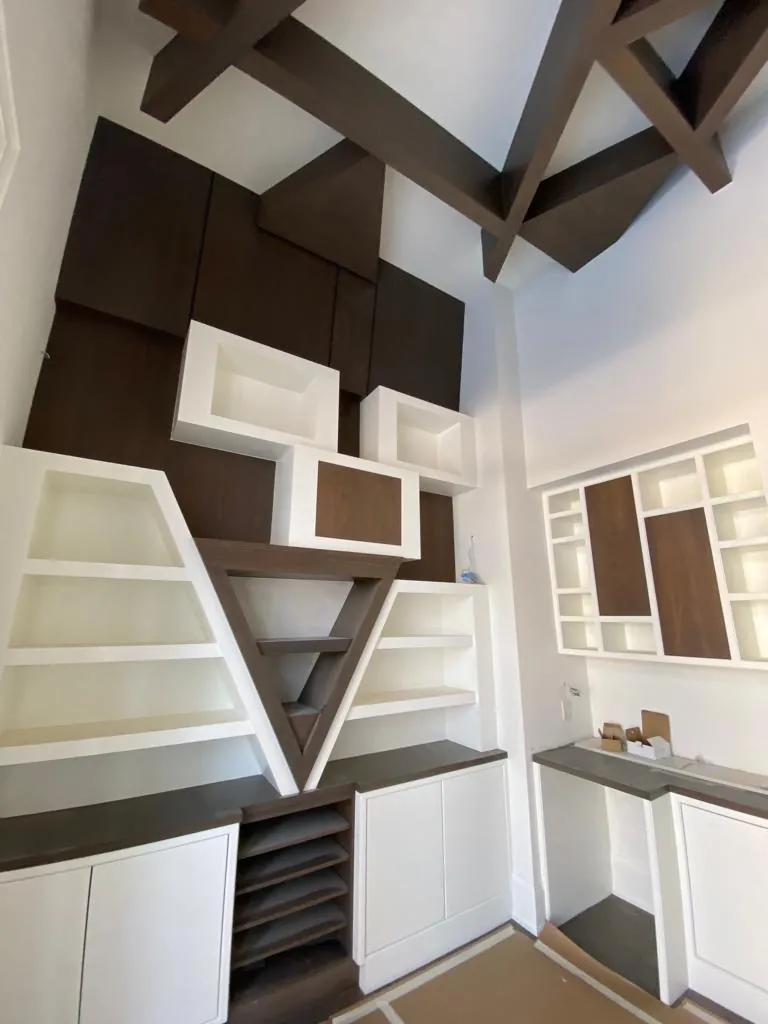Library wall of white shelves and walnut panels meeting in a V under exposed beams