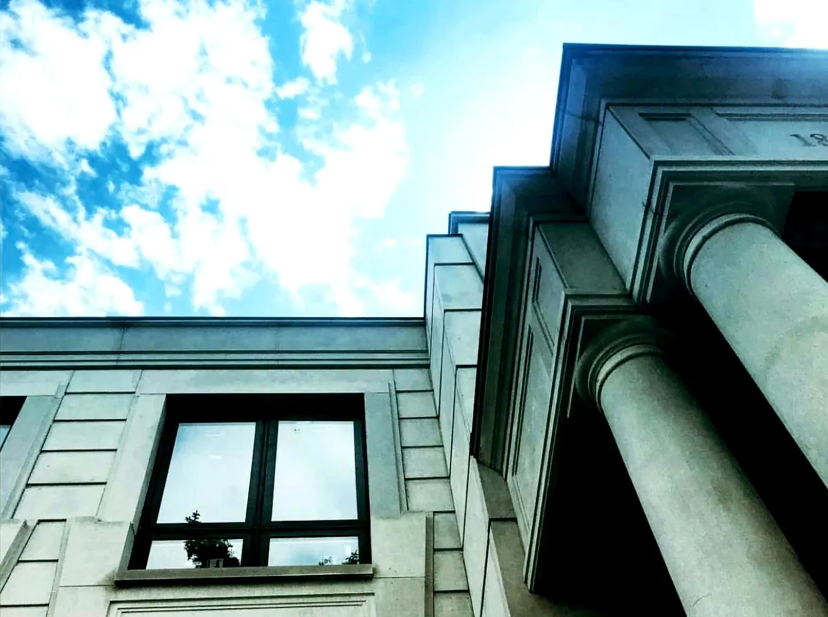 Low angle on limestone columns and a black-framed window against blue sky